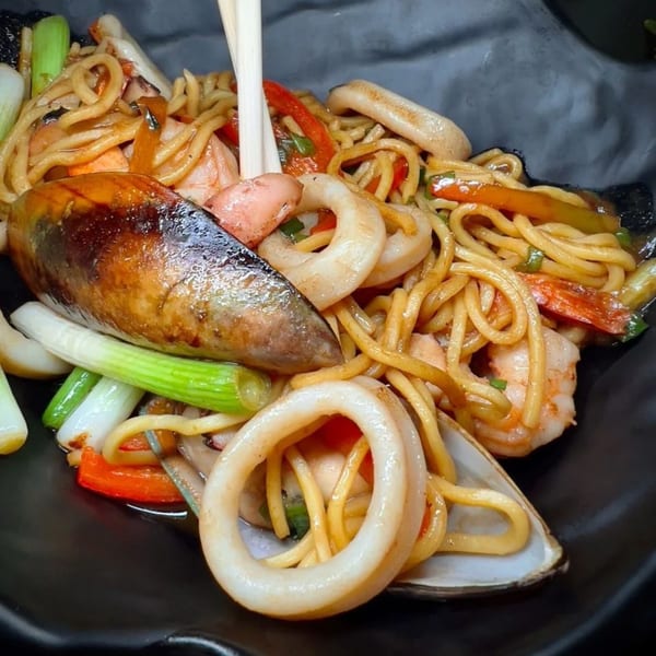 Peruvian seafood noodles with shrimp, squid, mussels, and vegetables, being served with chopsticks.