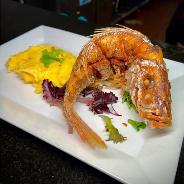 Whole fried red snapper with scrambled eggs and greens on a white rectangular plate.