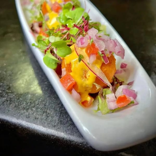 Peruvian appetizer in a white dish, featuring a yellow sauce, red onions, and microgreens.