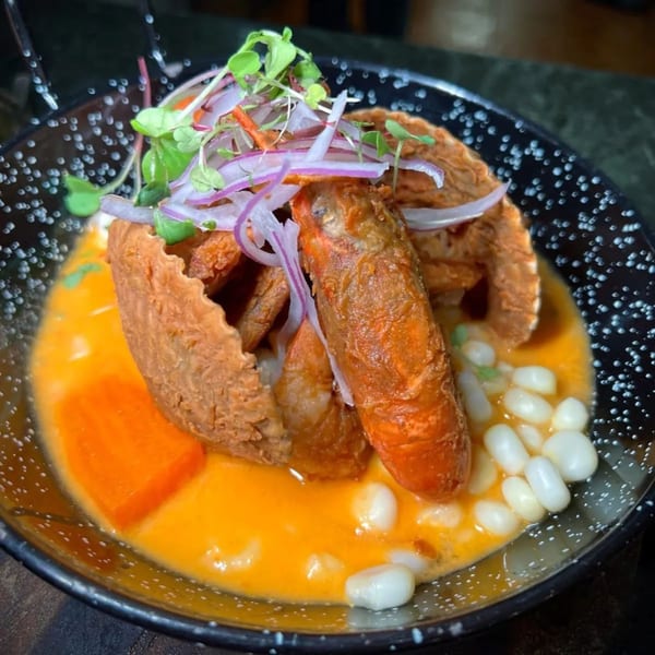 Peruvian dish with fried seafood, red onions, microgreens, corn, and sweet potato in a yellow sauce.