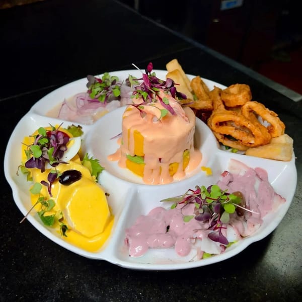 A white segmented platter holds various Peruvian dishes, including ceviche, causa, and fried calamari.