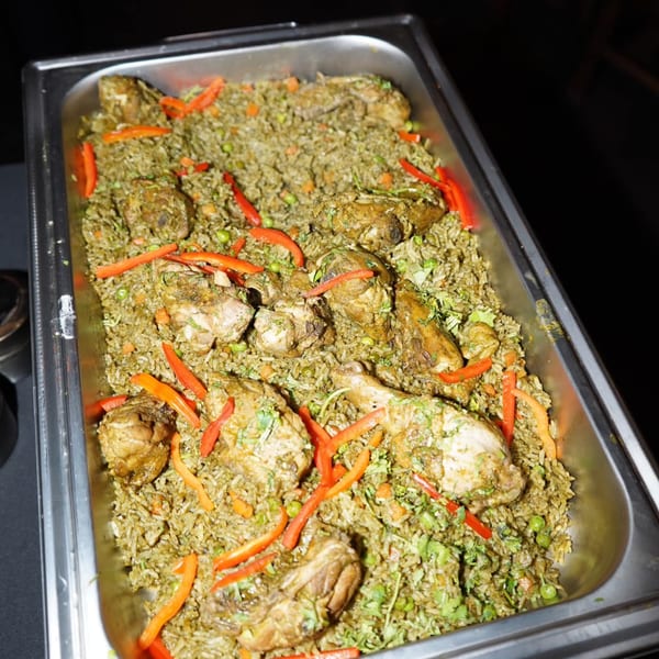 Peruvian Arroz con Pollo, a large tray of chicken and green rice with red pepper strips.