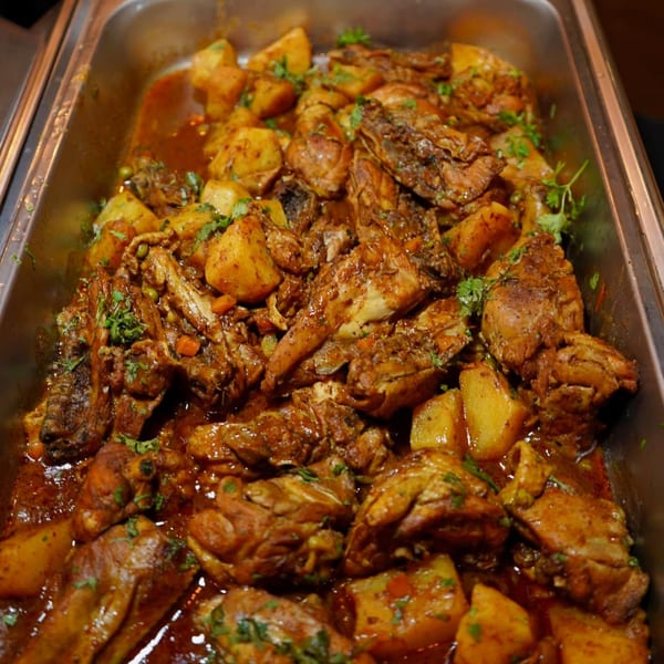 Peruvian aji de gallina, a creamy chicken stew with potatoes and cilantro, in a metal serving dish.