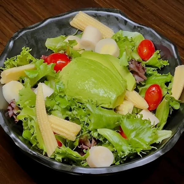 Peruvian salad with avocado, cherry tomatoes, baby corn, and hearts of palm in a black bowl.
