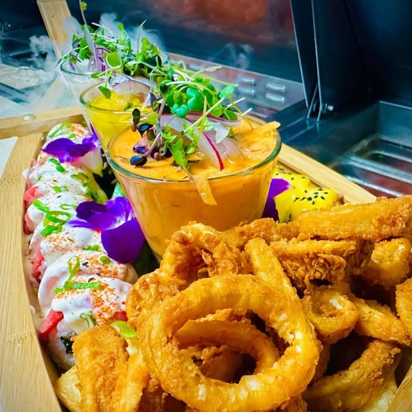 Peruvian sushi rolls, fried calamari, and onion rings with two sauces, garnished with edible flowers.
