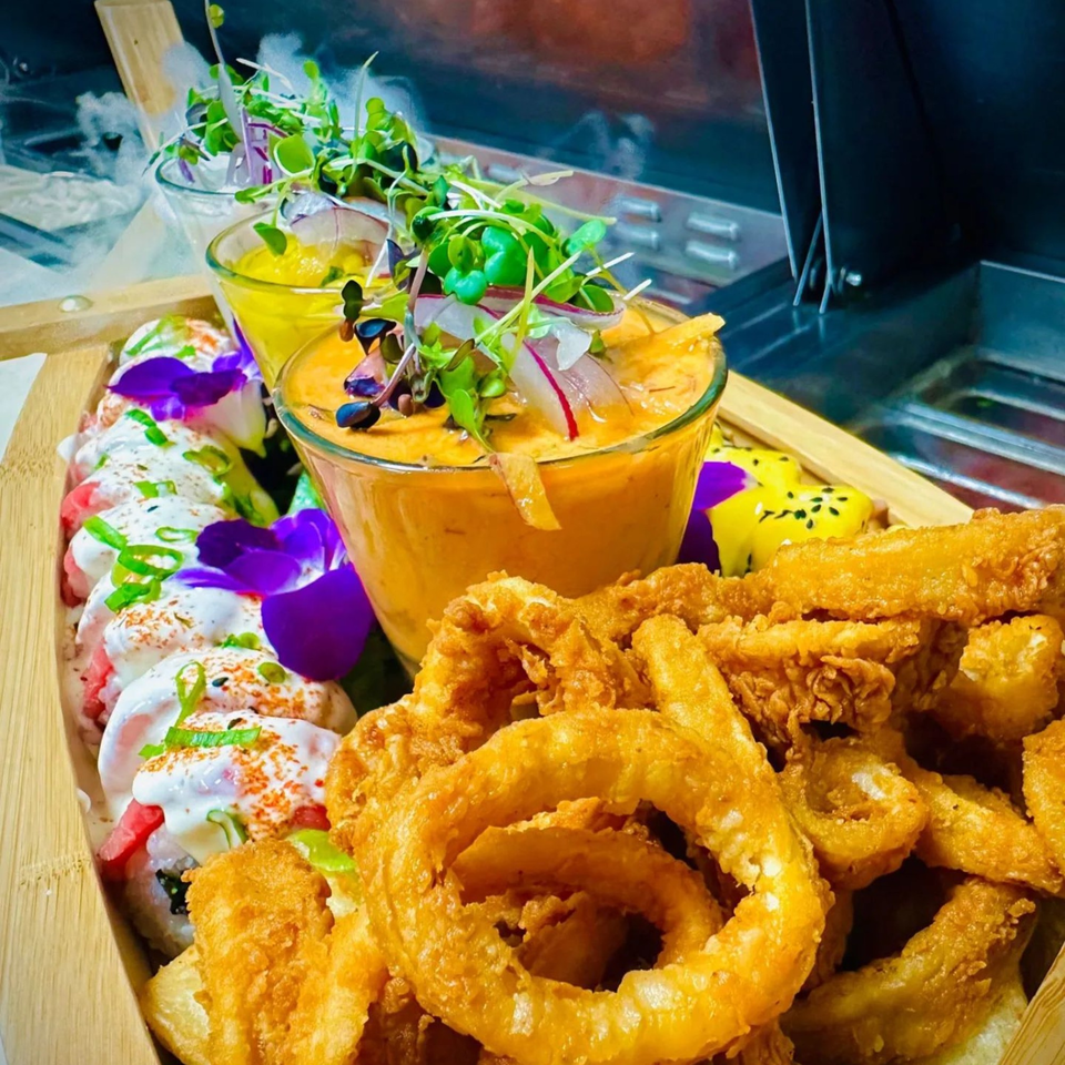 Peruvian sushi rolls, fried calamari, and onion rings with two sauces, garnished with edible flowers.